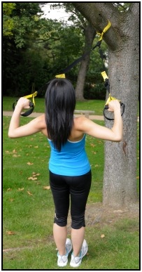 A woman doing a standing row with TRX fitness equipment.
